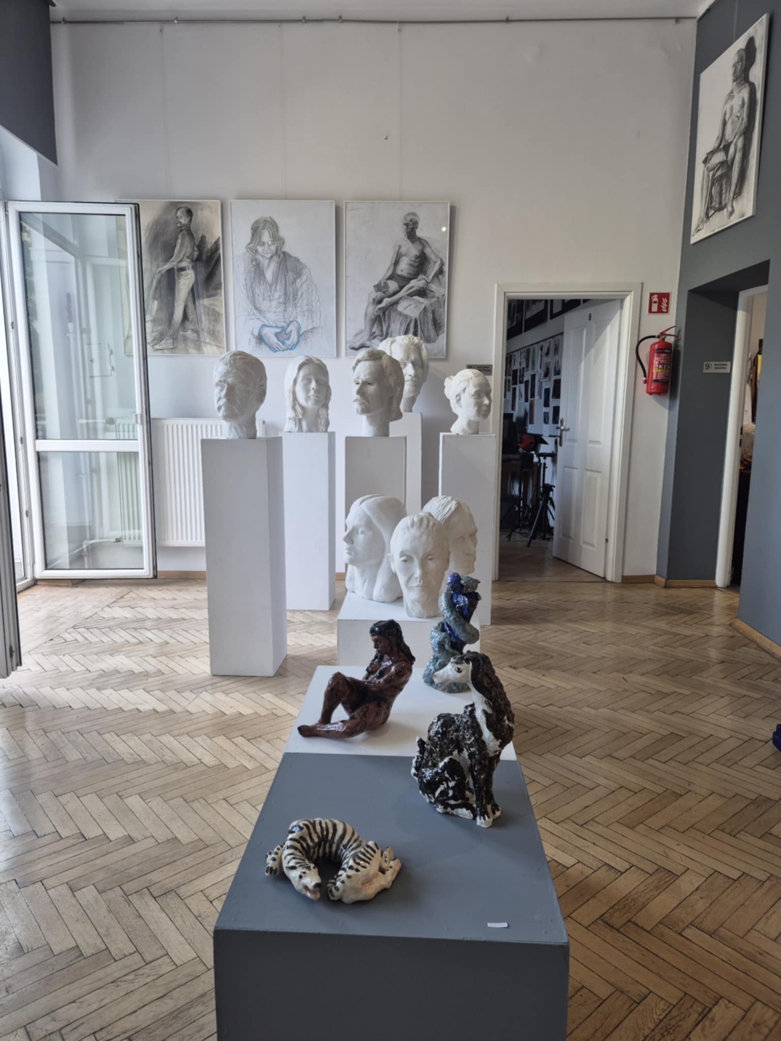 Głowy rzeźbiarskie na białych postumentach oraz ceramiczne formy przestrzenne na halu wystawowym.